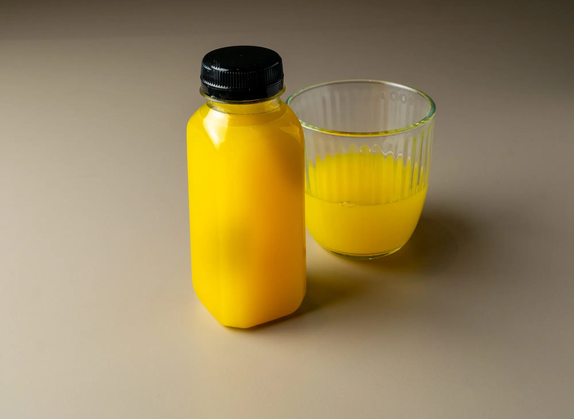 Zumo de naranja natural en botella, con un vaso al lado